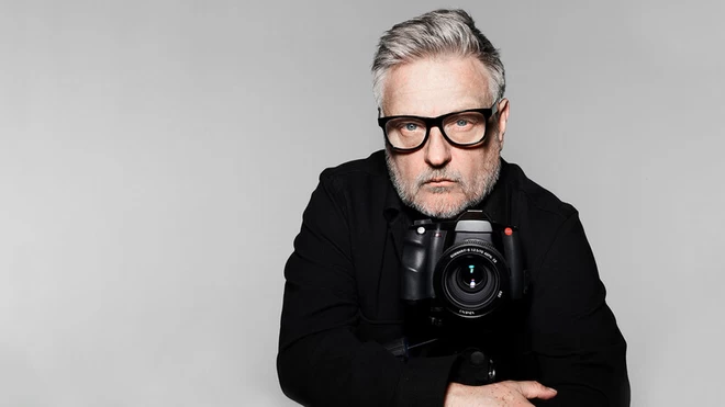 Rankin, photographer, director & humanitarian, looking at the camera, wearing black frames glasses and holding a camera