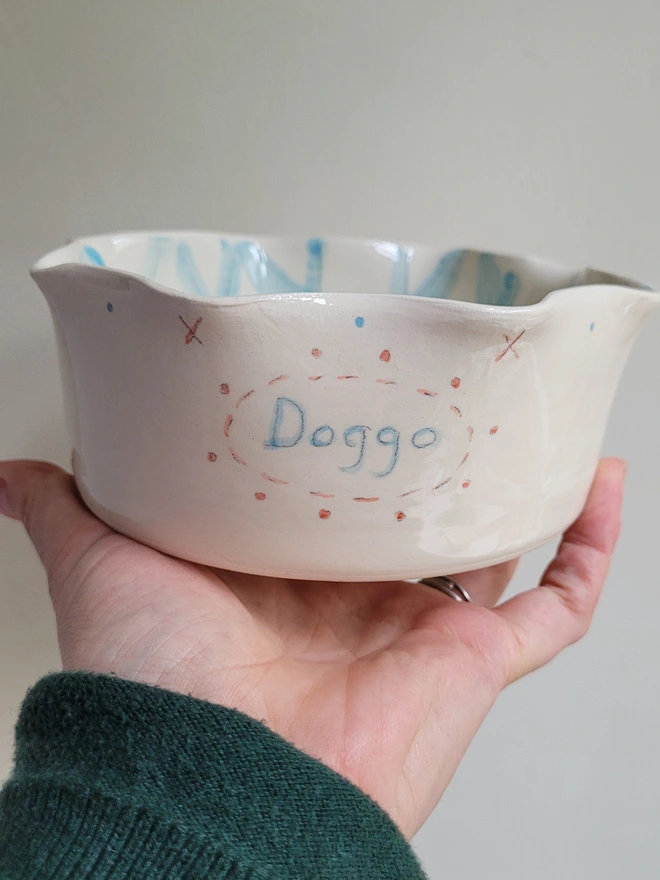 dog bowl held in a hand with the word doggo painted in blue with blue gingham check inside the dish