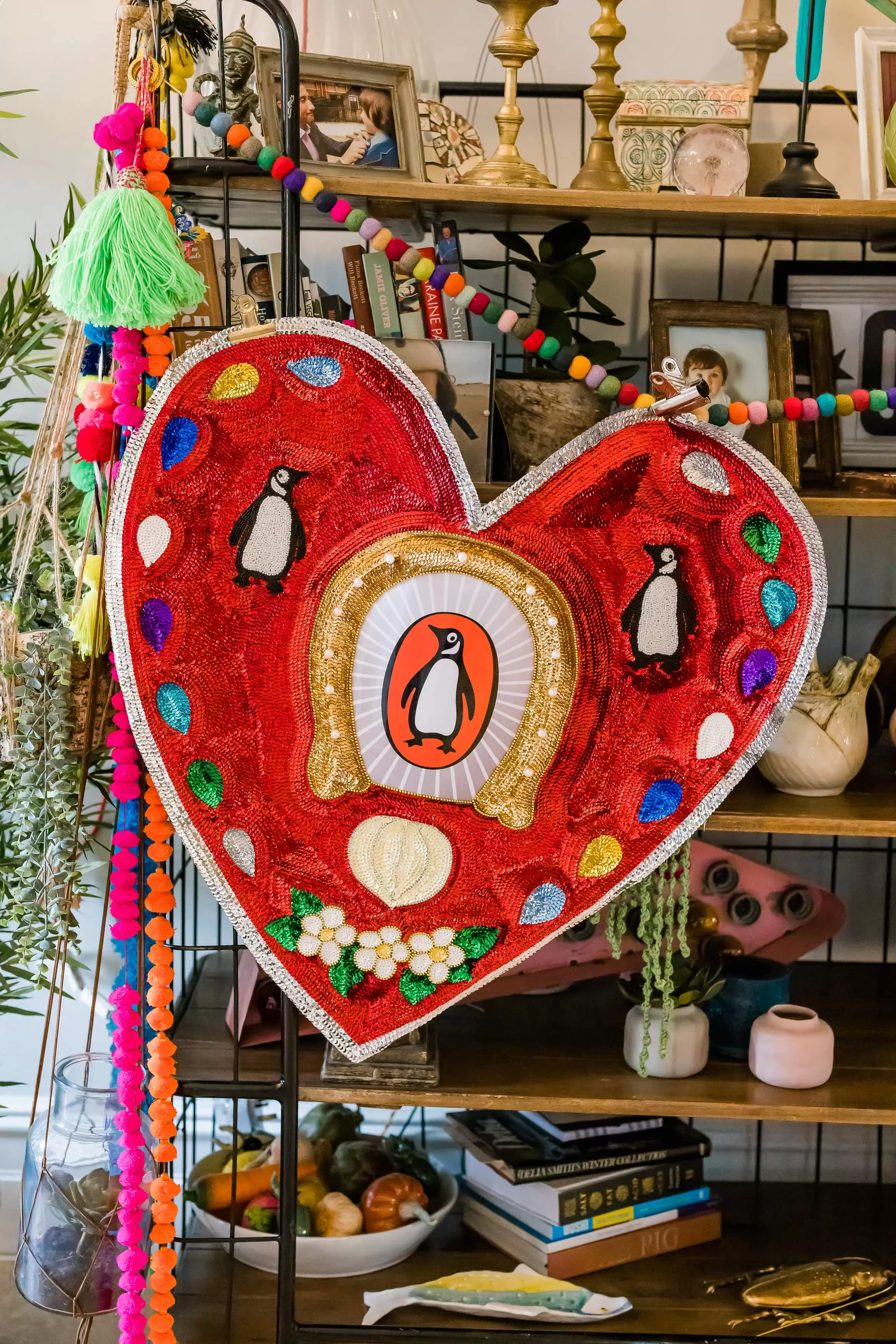 Red sequin heart with a penguin on it hanging off a bookcase 