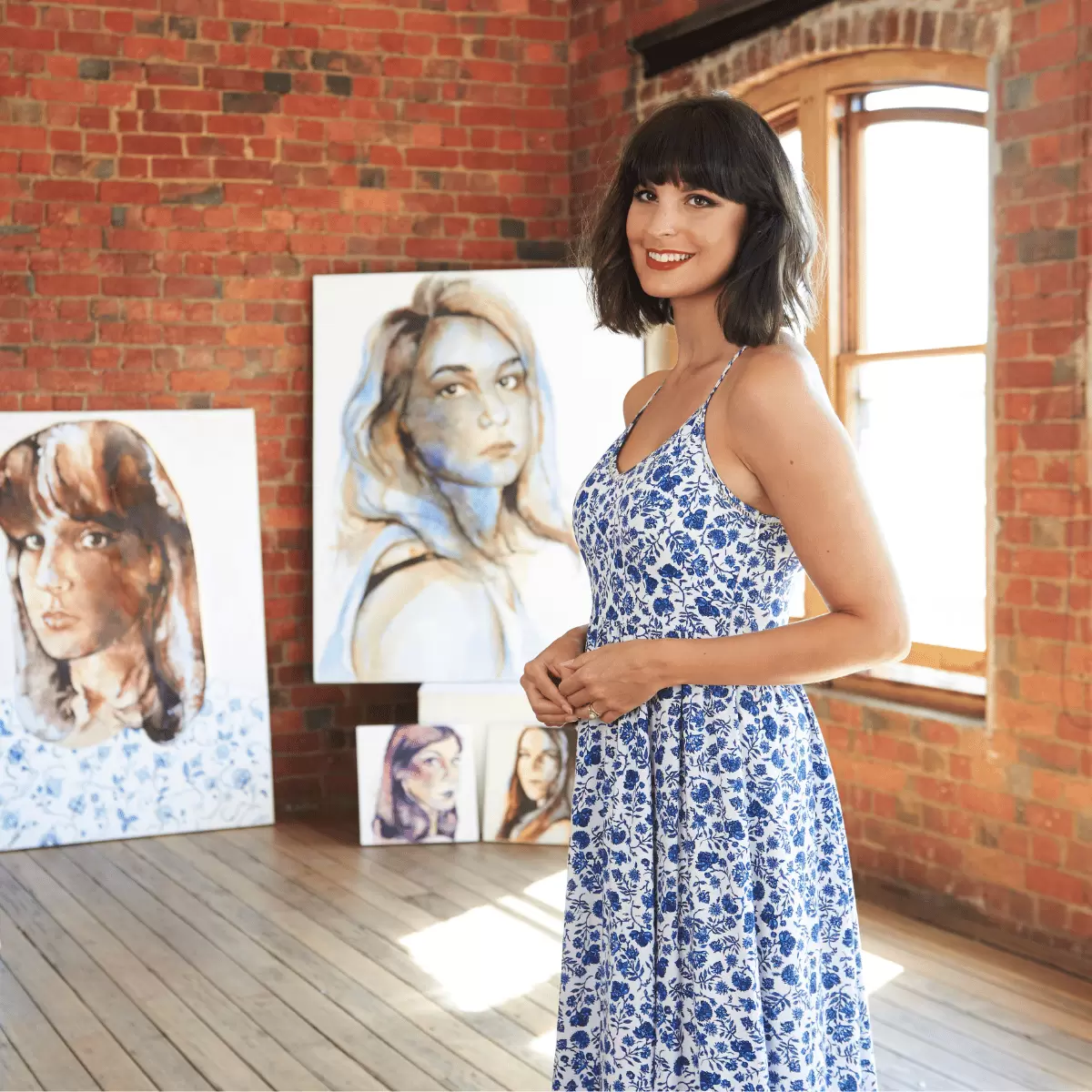 Johanna Wilbraham stands in a light-filled studio in front of a series of portraits.