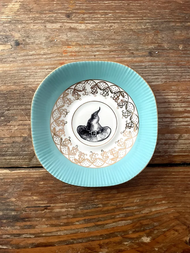 vintage plate with an ornate border, with a printed vintage illustration of a witch hat in the middle 