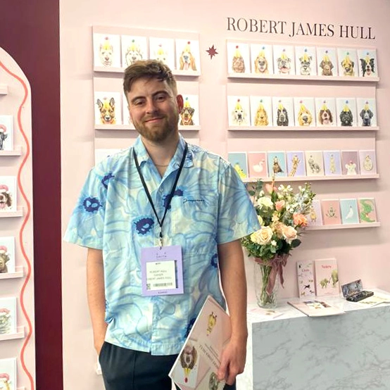 Robert James Hull posing in front of a selection of his dog and animal themed greeting cards