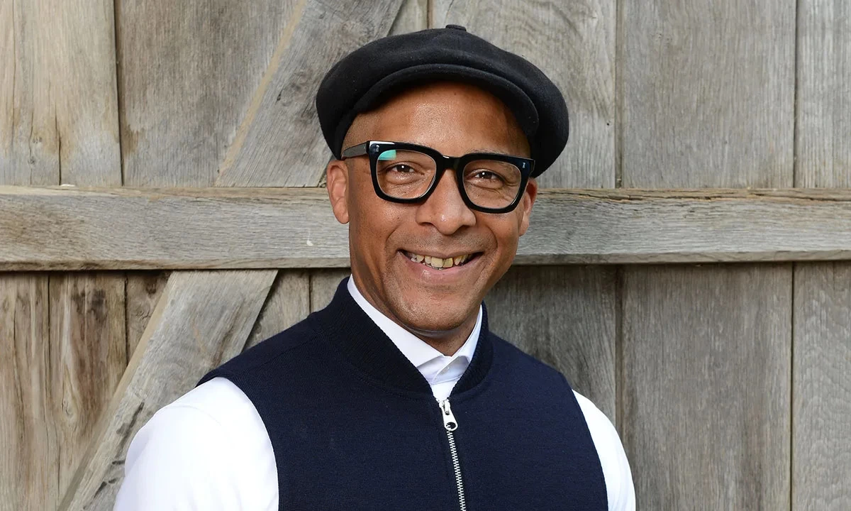 Jay Blades, founder of Jay & Co, smiling at the camera wearing a navy baker boy hat.