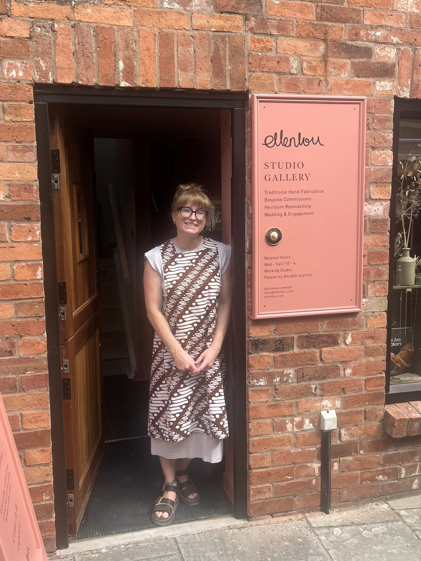 Artisan jeweller and maker Ellie standing warmly inside the doorway of her Shropshire studio gallery.