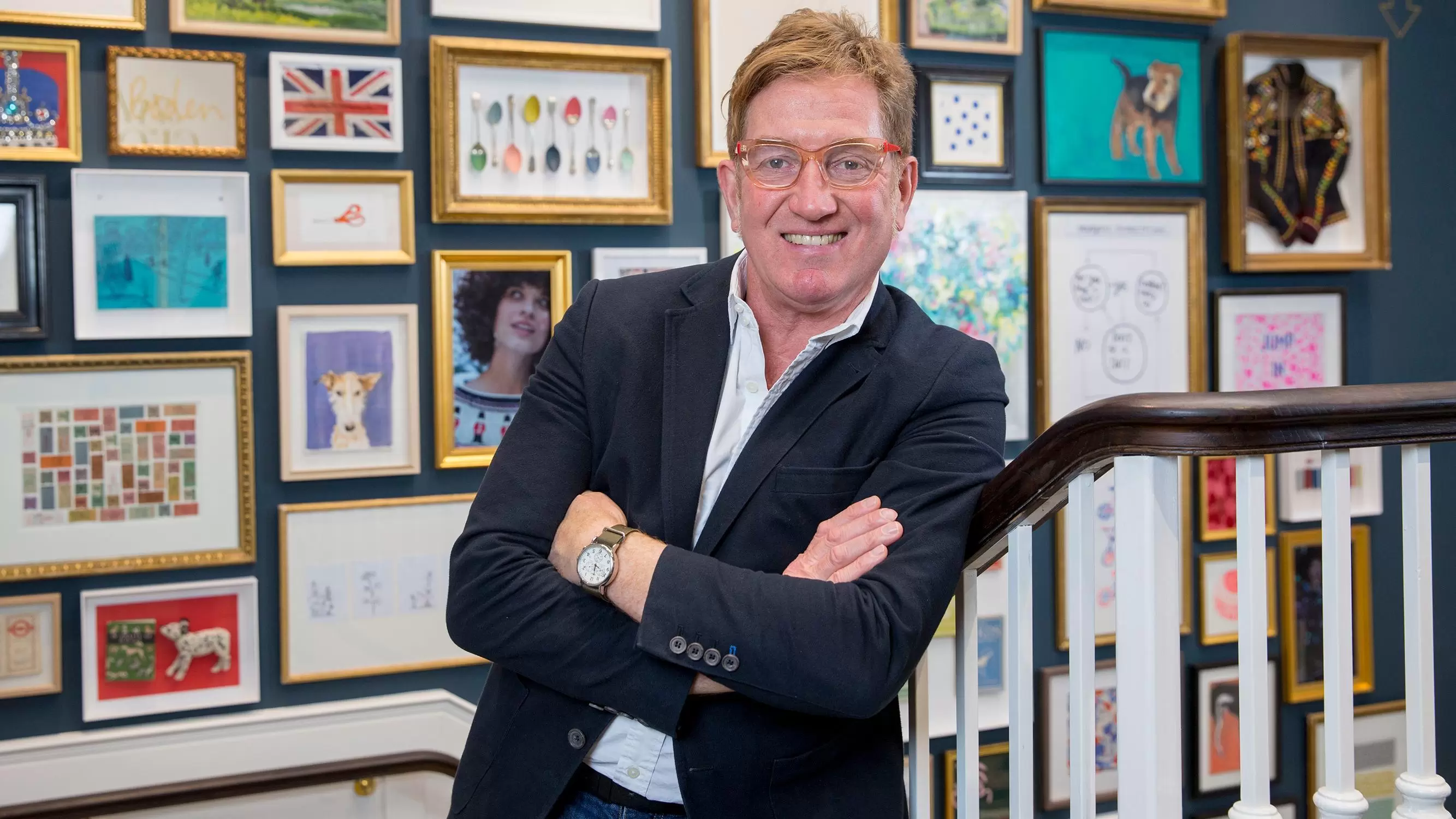 Johnnie Boden CBE, founder of Boden, leaning against a staircase with his arms crossed. 