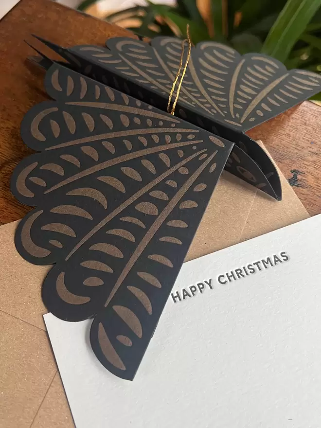 Black and gold printed bird decoration with wings folded out. Sitting on 'Happy Christmas' letterpress printed notecard.  