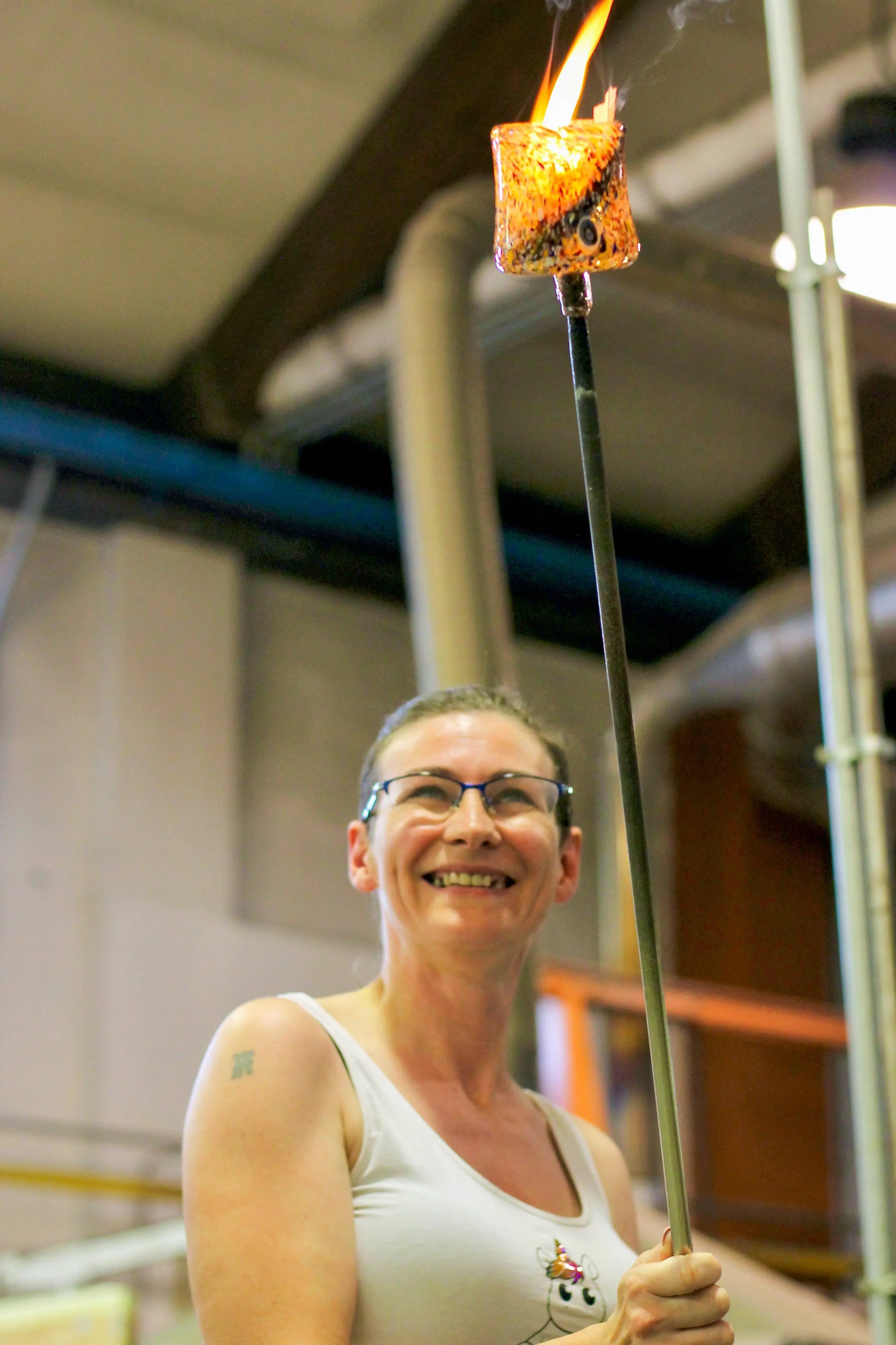 Scarlet holding a glass vessel on the end of a blow tube in a hotshop