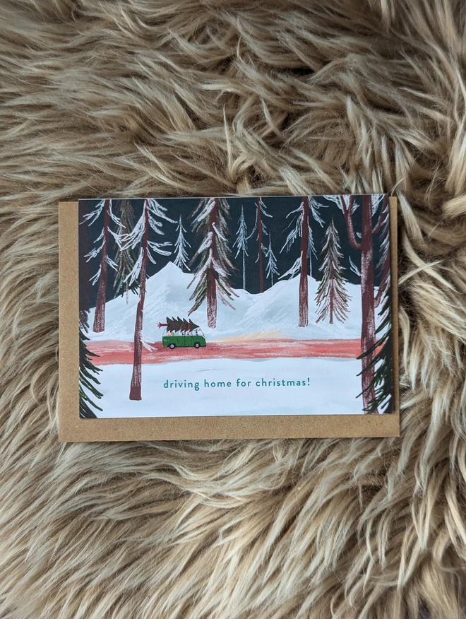 Driving home for Christmas card, shows a camper van carrying a Christmas tree through a forest.