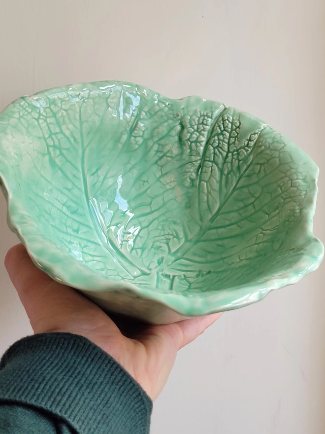a green pottery serving bowl with cabbage leaves imprinted held in a hand