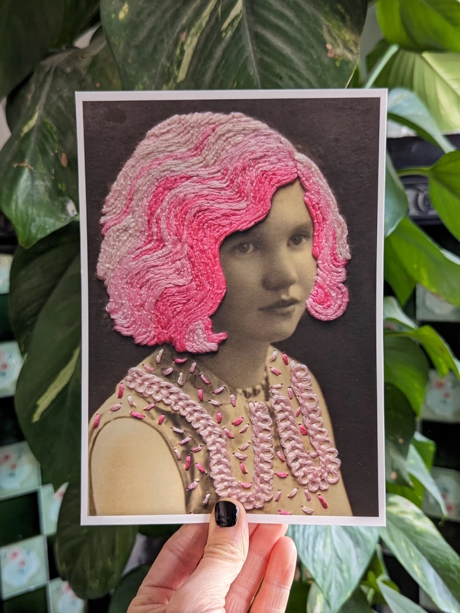 Print of B&W girl, with embroidered pink hair and dress held in front of plant