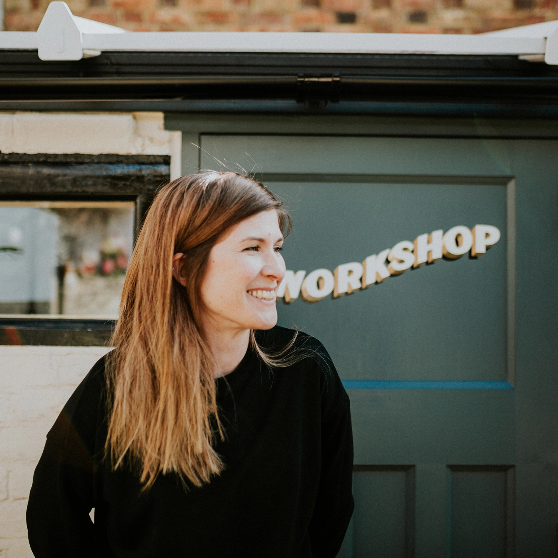 Esther North AKA Sylvie Signs standing in front of her workshop, smiling. 