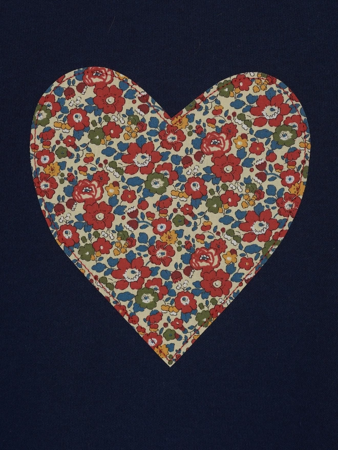 A close up of a liberty floral fabric heart sewn on to a navy t-shirt
