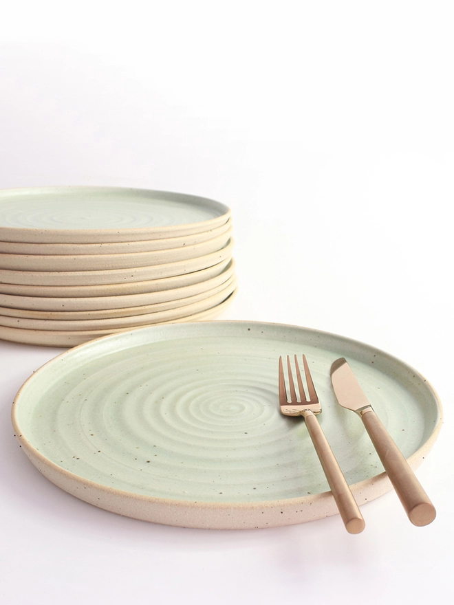 Green dinner plate in foreground with cutlery, stack of plates in background