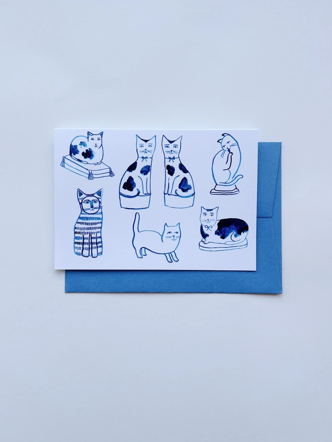 An illustrated greeting card featuring ink drawings of ceramic cats with a pale blue envleope