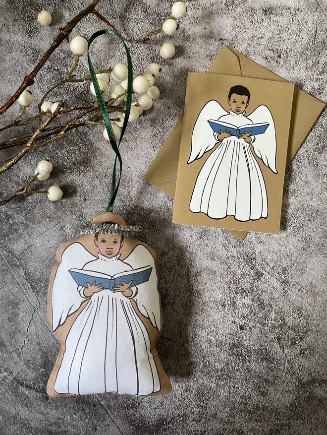 a boy angel decoration next to a matching greeting card featuring an afro Caribbean boy angel