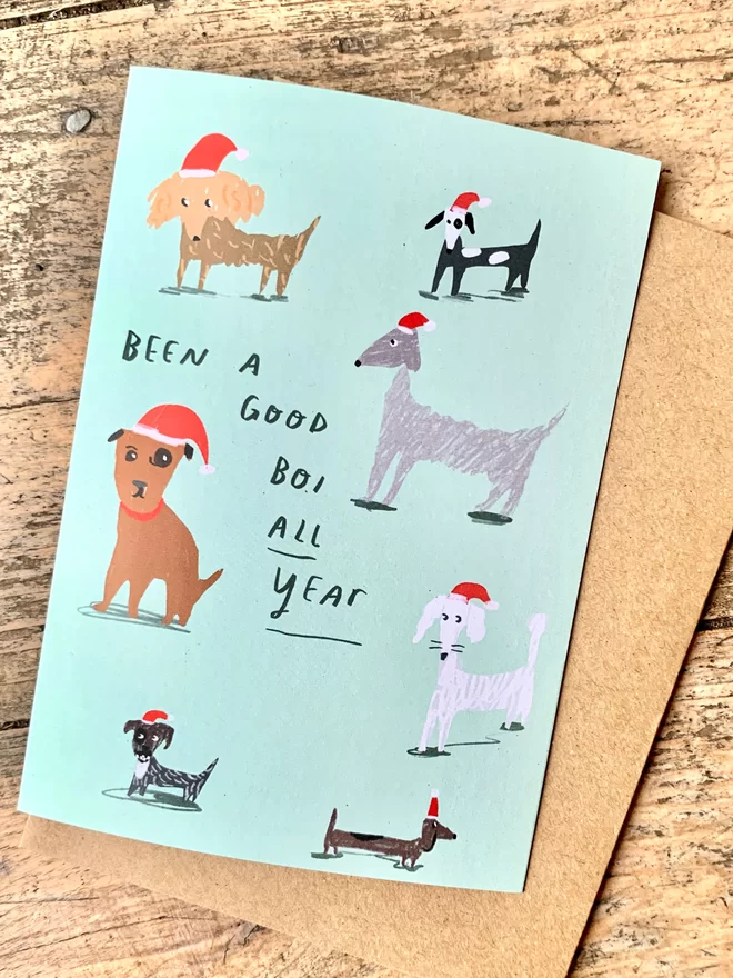 Mint green background with scribbled drawings of different dogs all wearing santa hats, reads 'been a good boi all year'