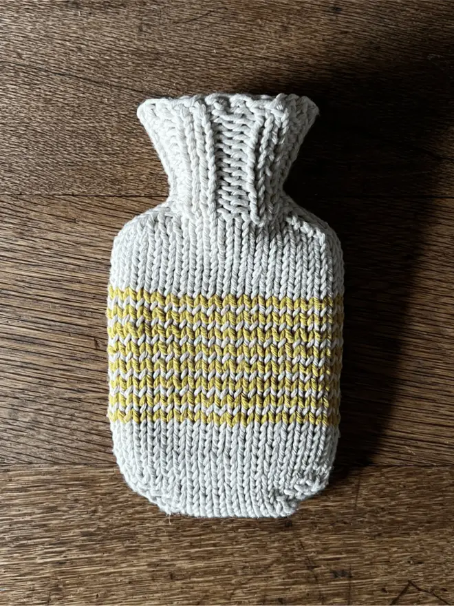 Mini Hot Water Bottle with yellow striped knitted string cover on an oak table