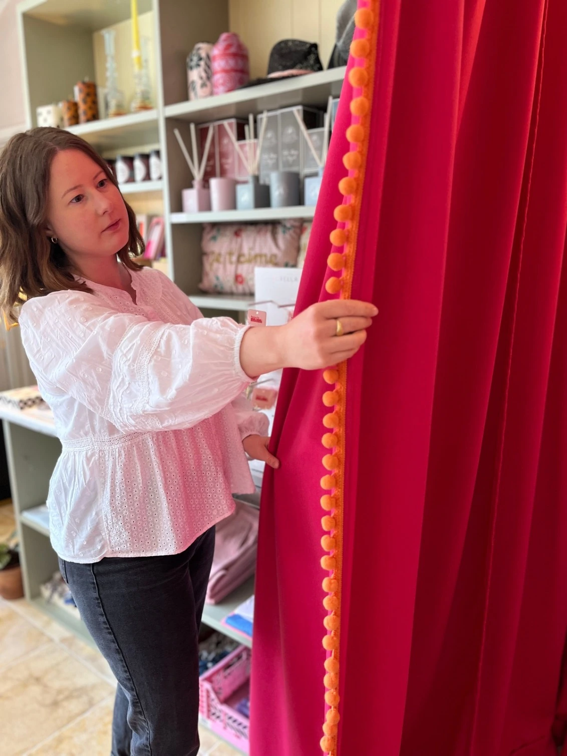 Founder of Annabel Wond Interiors pictured with a bespoke handmade curtain made for a boutique shop in hot pink with pom poms