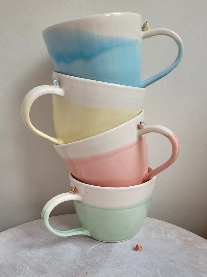 a stack of bright pastel glazed handmade pottery cups with robin birds or blue tit on the handle