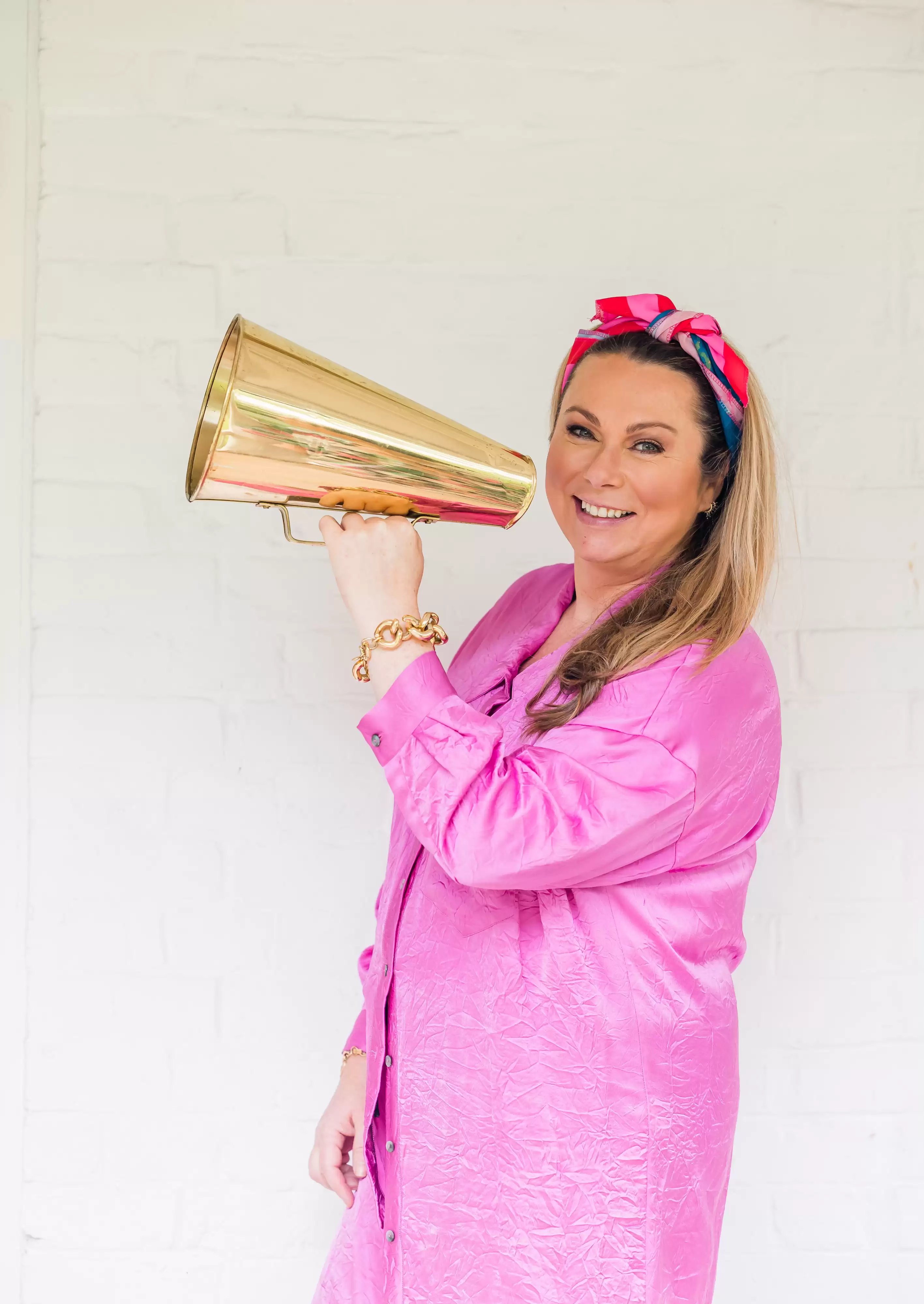 Holly Tucker holding a gold megaphone wearing a pink outfit 