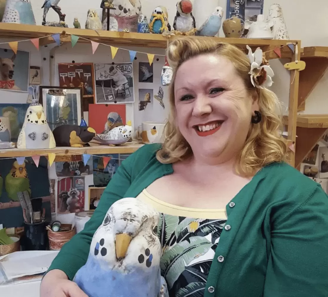 Charlotte Miller sitting in her studio holding a ceramic bird 