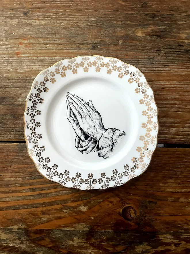 vintage plate with an ornate border, with a printed vintage illustration of praying hands in the middle 