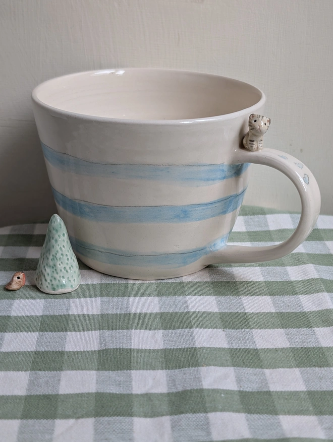 pottery cup with blue stripes and a tiny ceramic cat on the handle