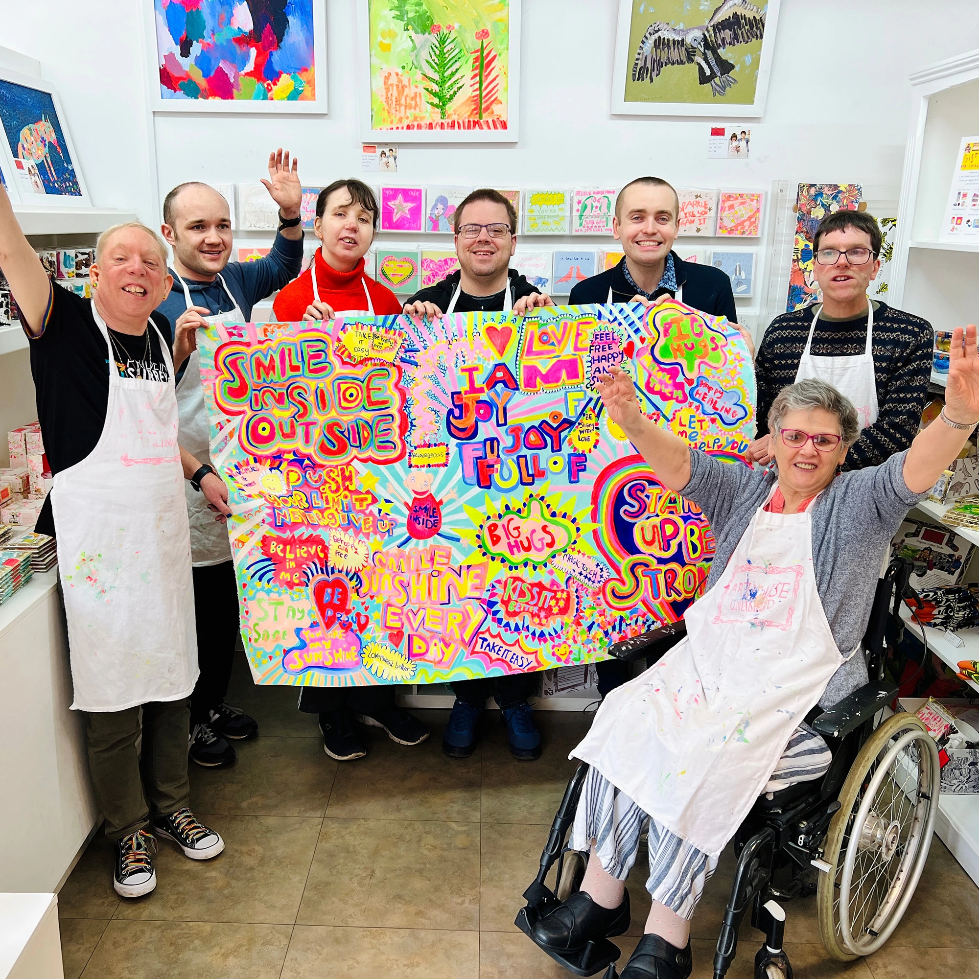 7 Happy artists holding colourful Full of Joy original charity artwork in Arthouse Unlimited shop