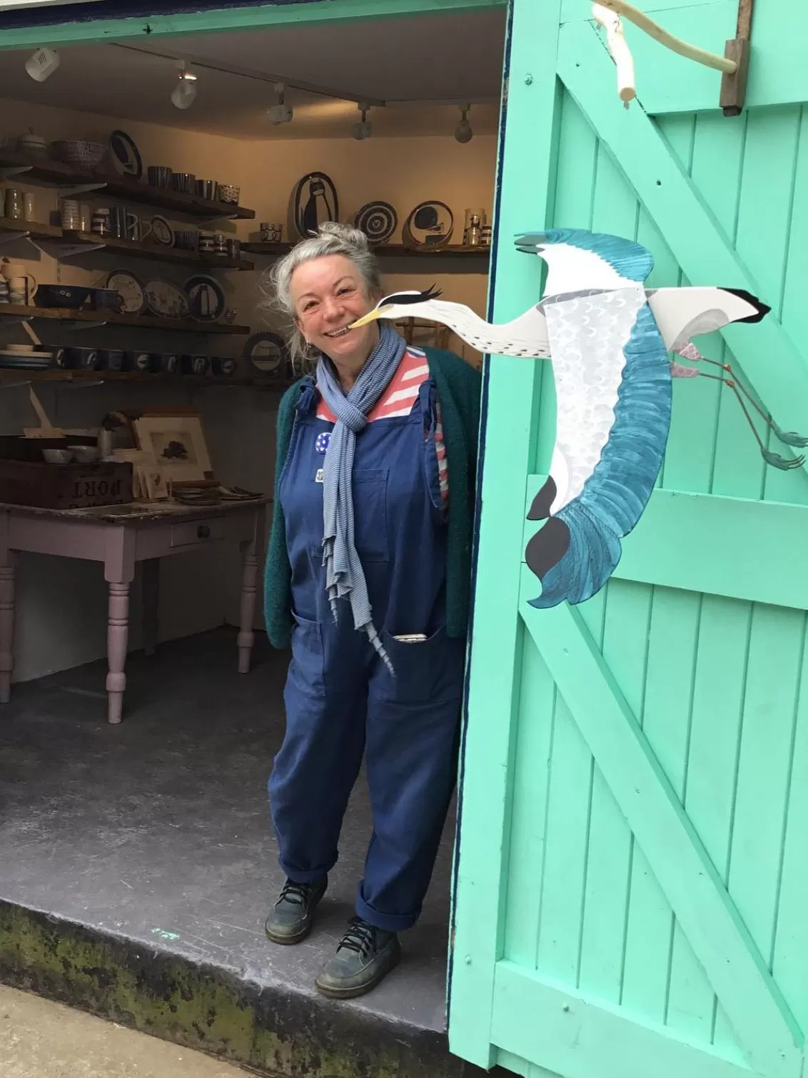 Founder Philippa standing in her workshop looking out at the camera with one of her crane flying bird products outside