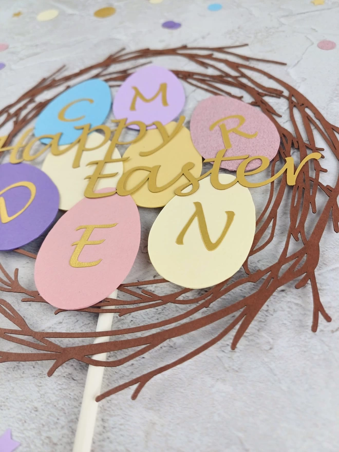 Closeup of paper easter egg shapes each with a different initial cut from gold paper
