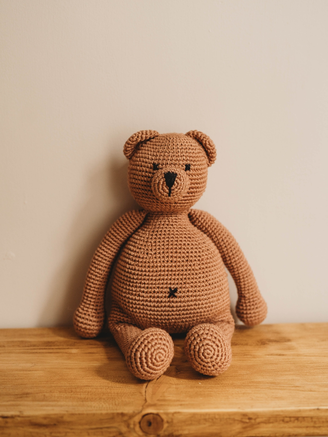 handmade brown crochet teddy bear on wooden shelf