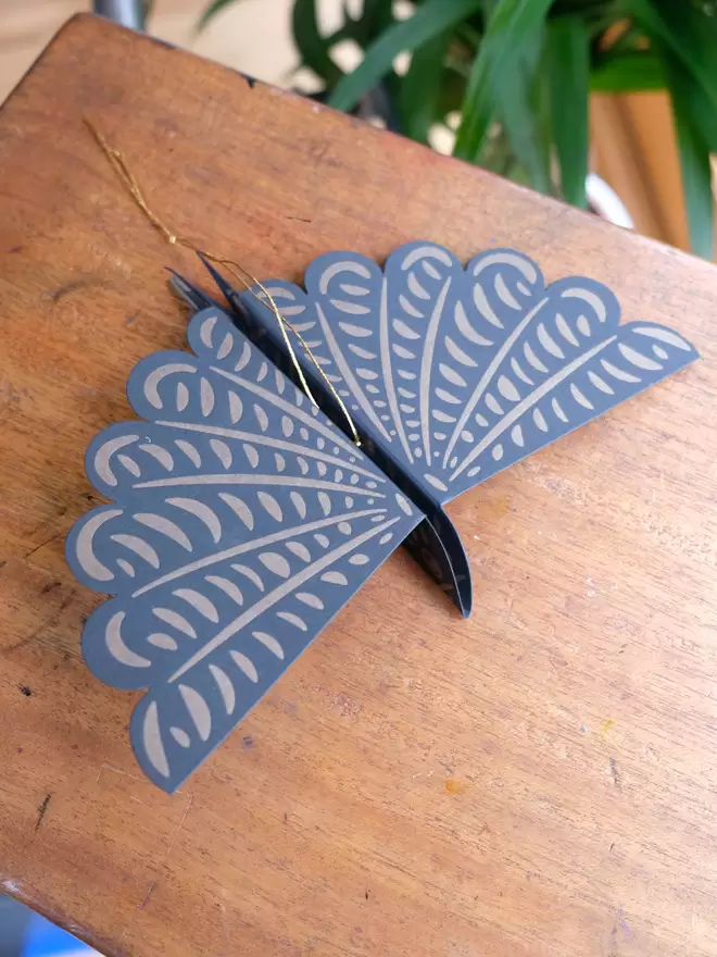 Black paper bird, printed with gold ink illustration. Sitting on wooden top.