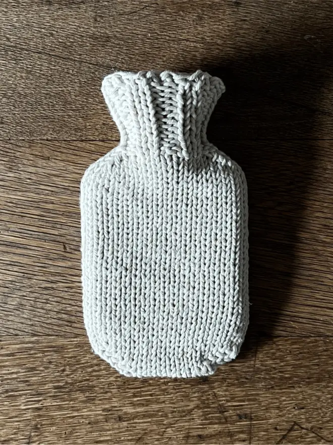 Mini Hot Water Bottle with knitted string cover on an oak table