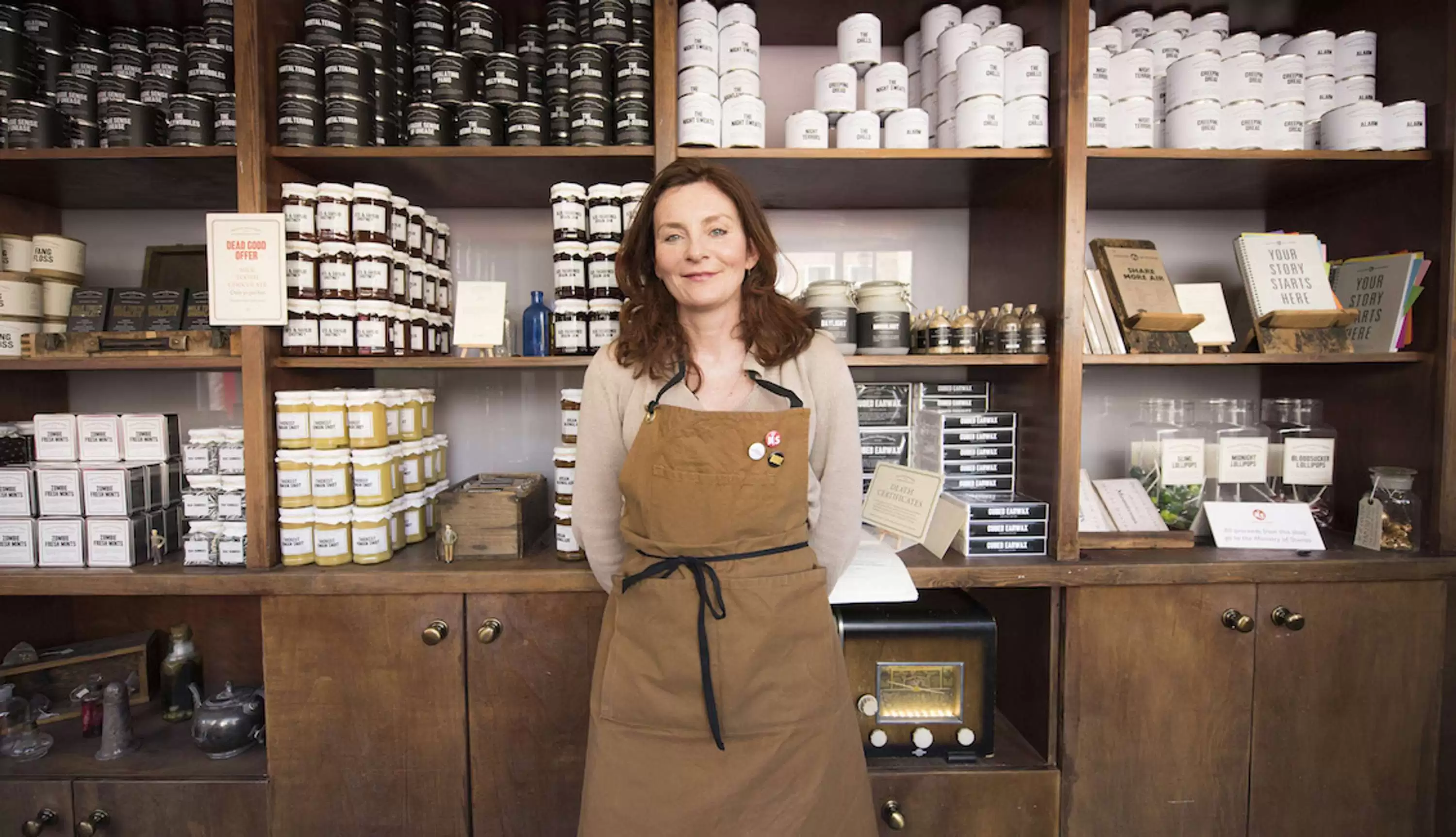 Woman standing in a store with product on shelves behind her 