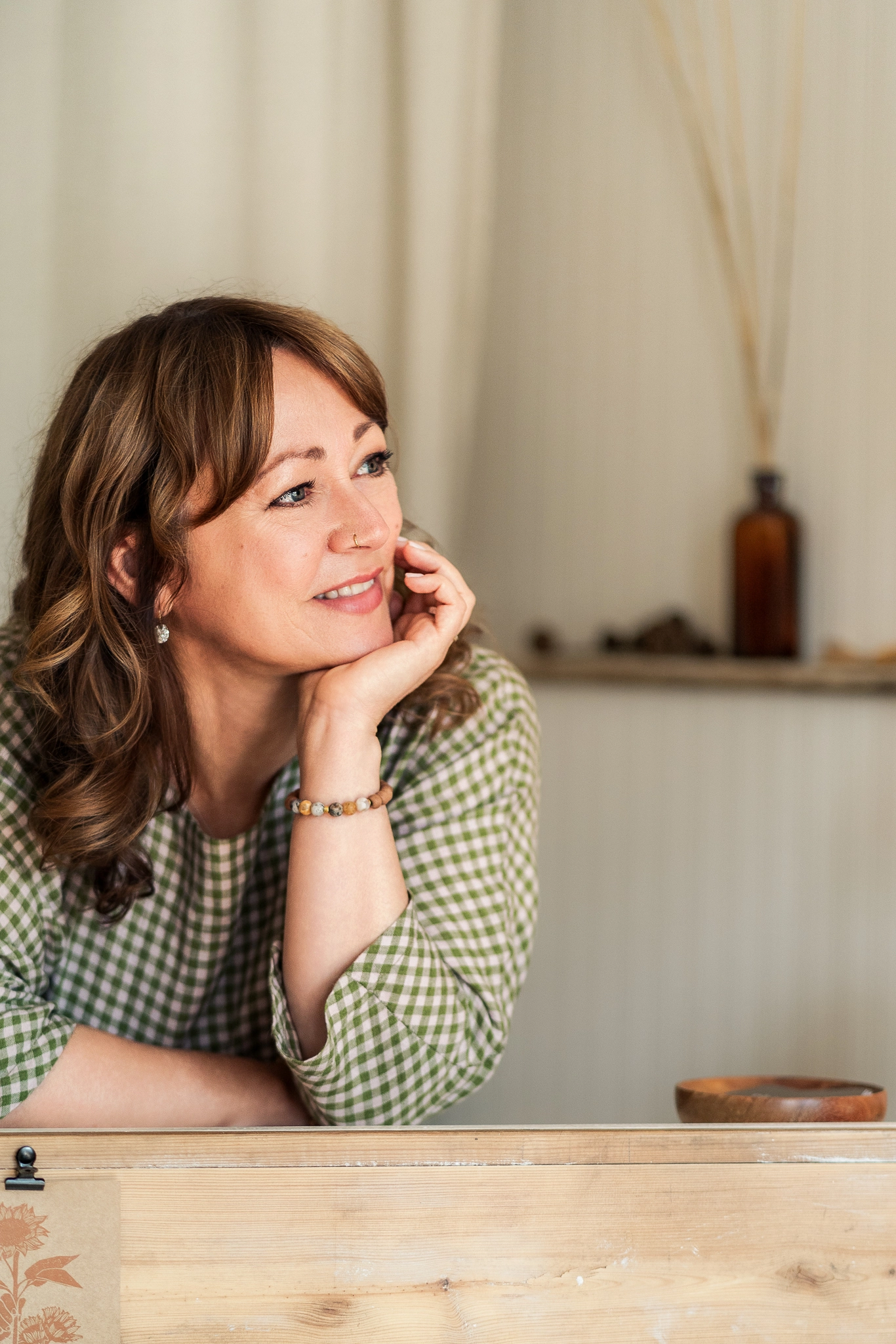 woman wearing a green gingham dress casually leaning on her shop counter