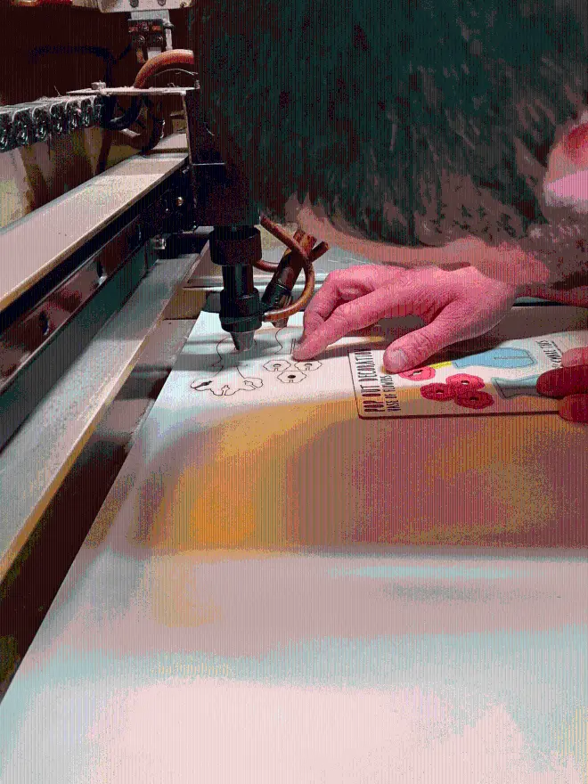 A man standing over a laser cutting machine looking at the flower decorations that he has laser cut