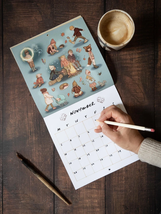 photo of a calendar open on the month of November featuring illustrations of children and a hand writing coffee cup and ink pen