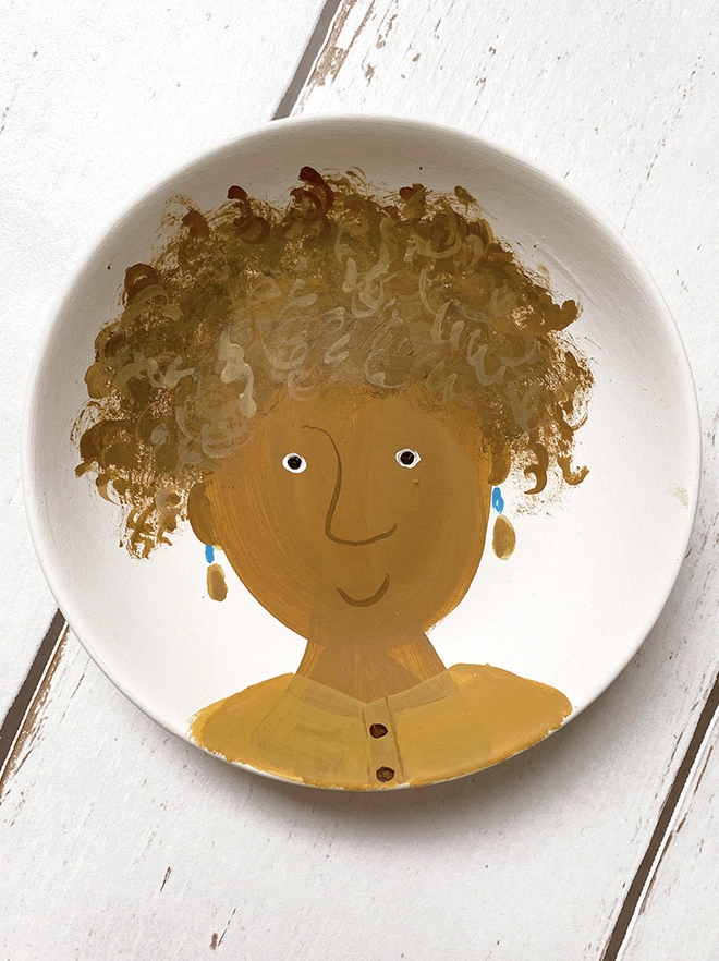 small white plate with stylised painted portrait of girl with ochre coloured shirt