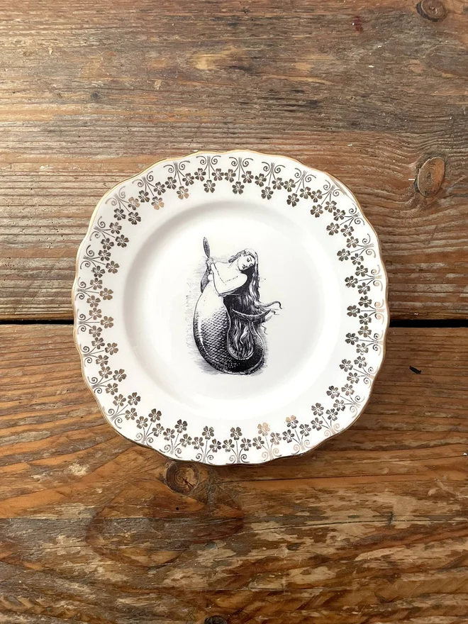 vintage plate with an ornate border, with a printed vintage illustration of mermaid in the middle 