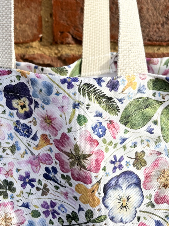 Close-up of a shopping tote with floral print design and beige webbed handles.
