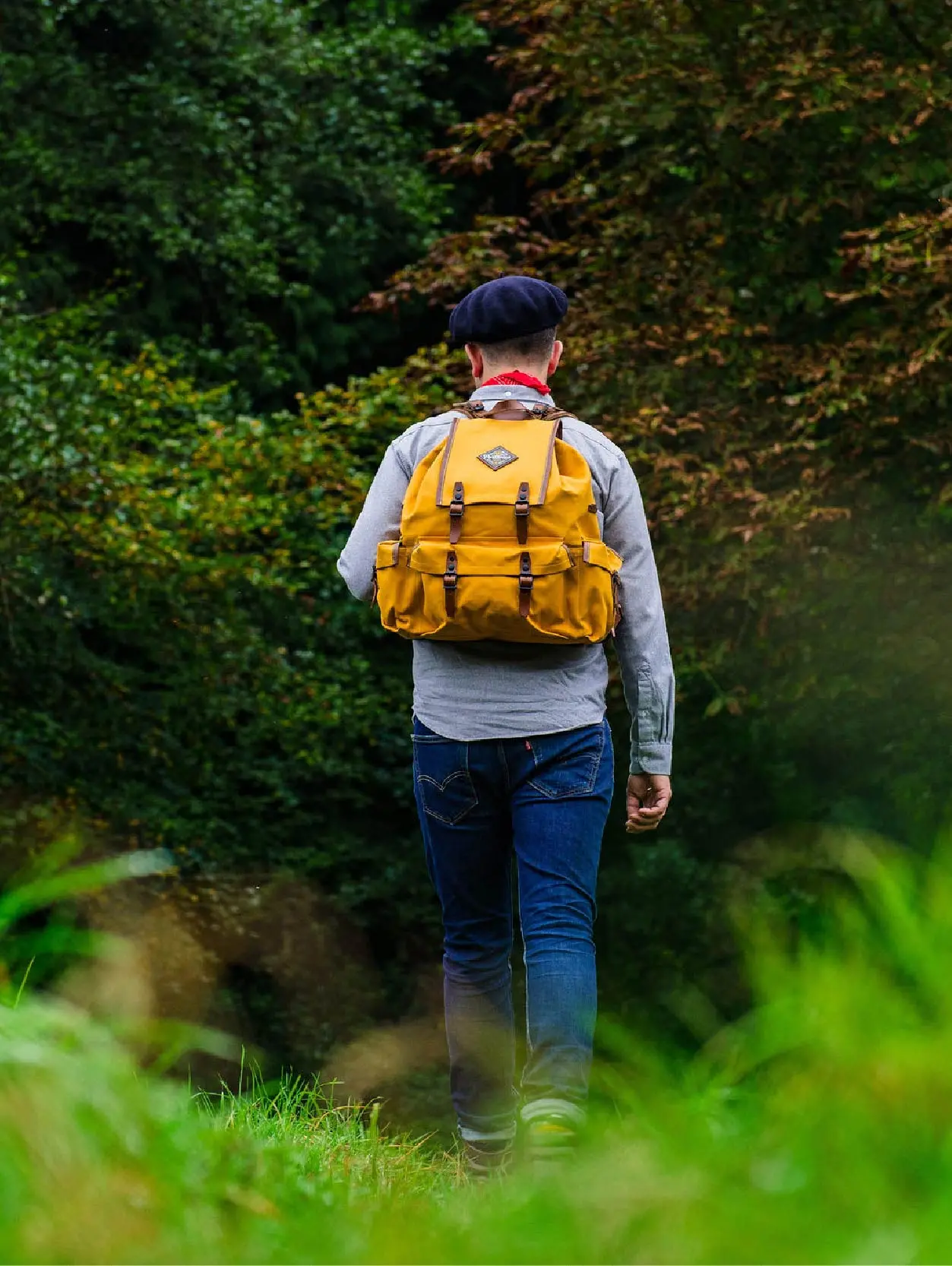 Model wearing Yellow Rockness frame backpack walking through long grass towards trees.