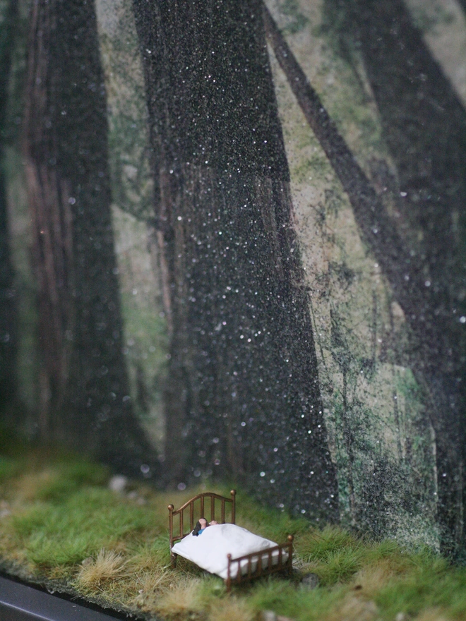 A diorama showing a mother and daughter snuggling in bed in a forest