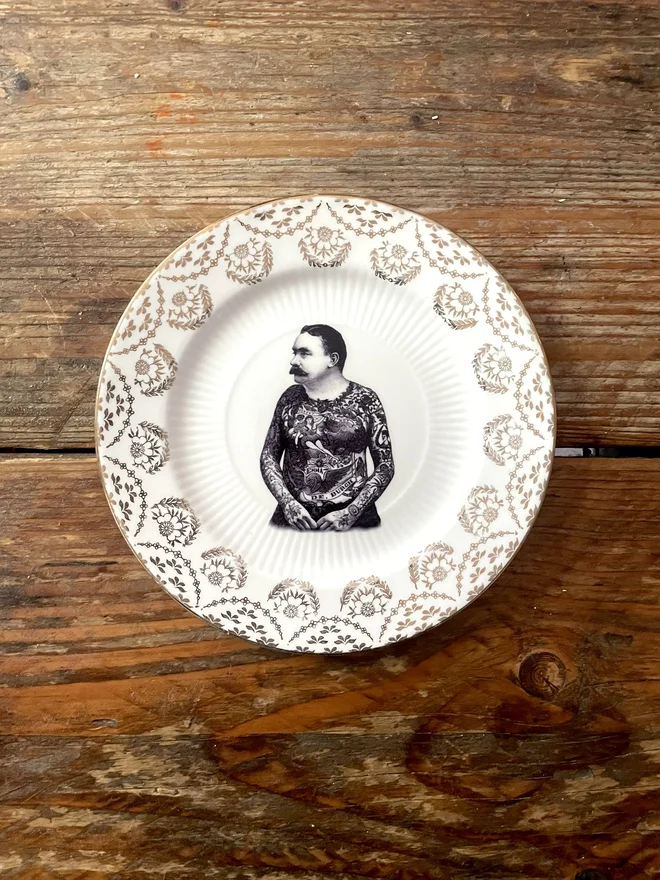 vintage plate with an ornate border, with a printed vintage illustration of a tattooed man in the middle 