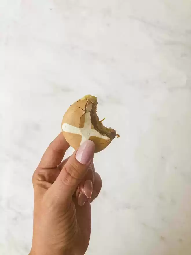 a hand holding a half eaten hot cross bun macaron