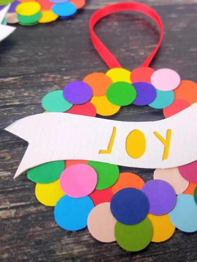 Colourful Christmas Bauble "Joy" papercut in yellow on a white banner  closeup
