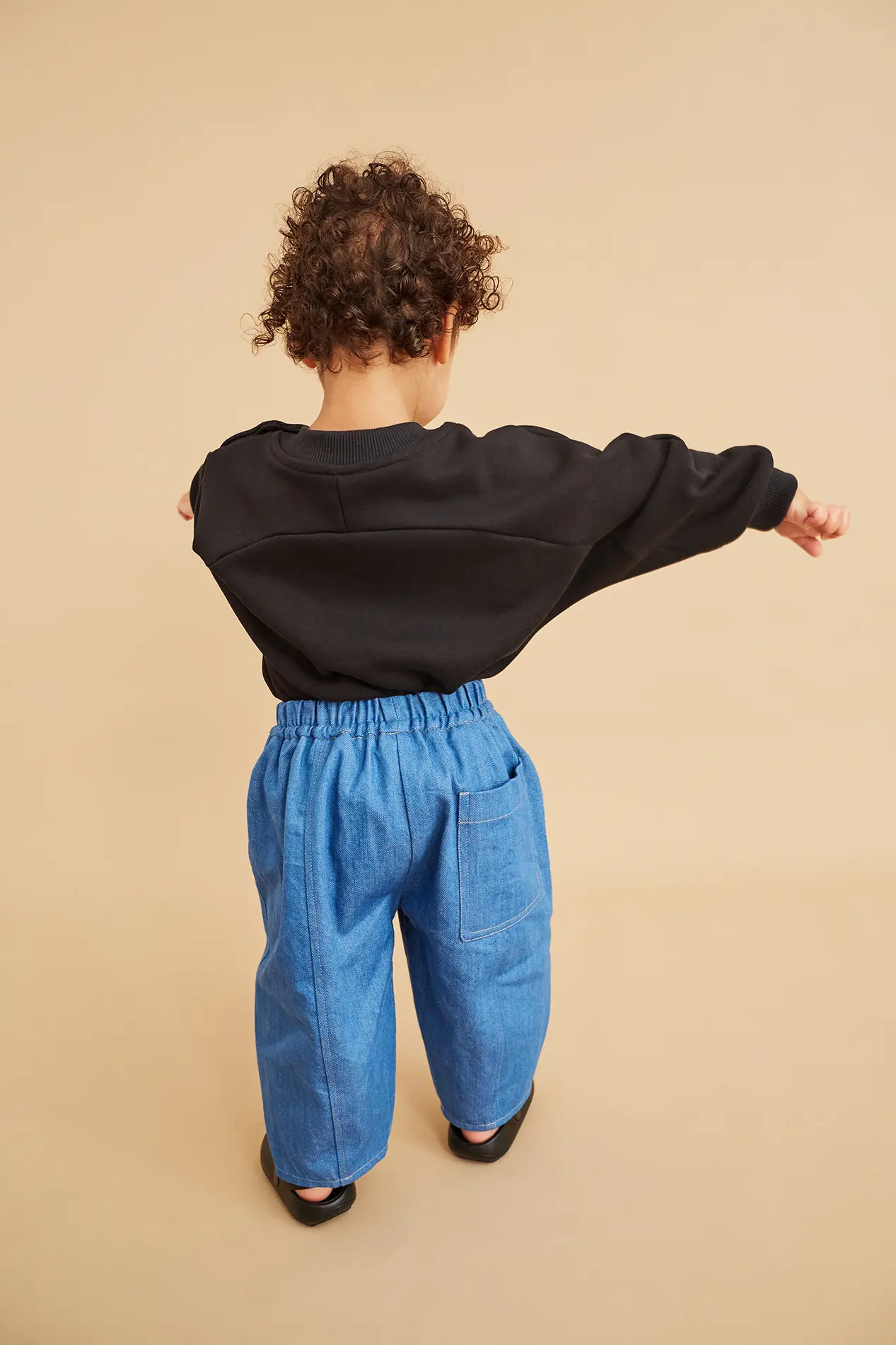 Studio koter model posing in balloon shaped organic denim trousers and oversized romper. She is a toddler aged about two years old.