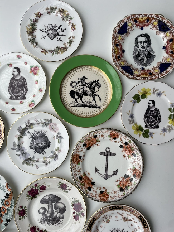 an eclectic collection of vintage plates hung together on a white wall, each plate is different with patterned or gold borders and vintage images in their centres