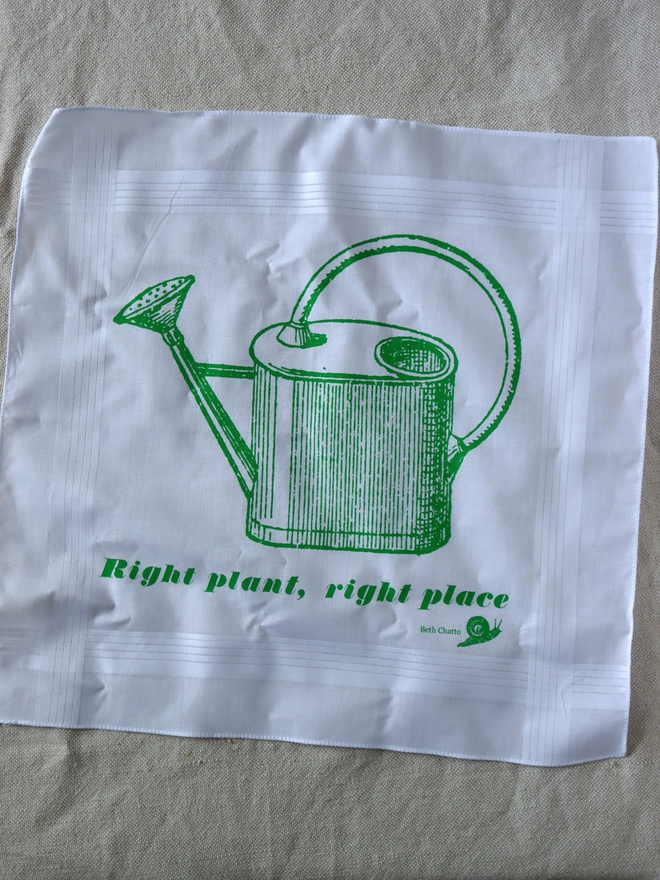 A Mr.PS Gardern Watering Can printed handkerchief laid flat on a linen tablecloth