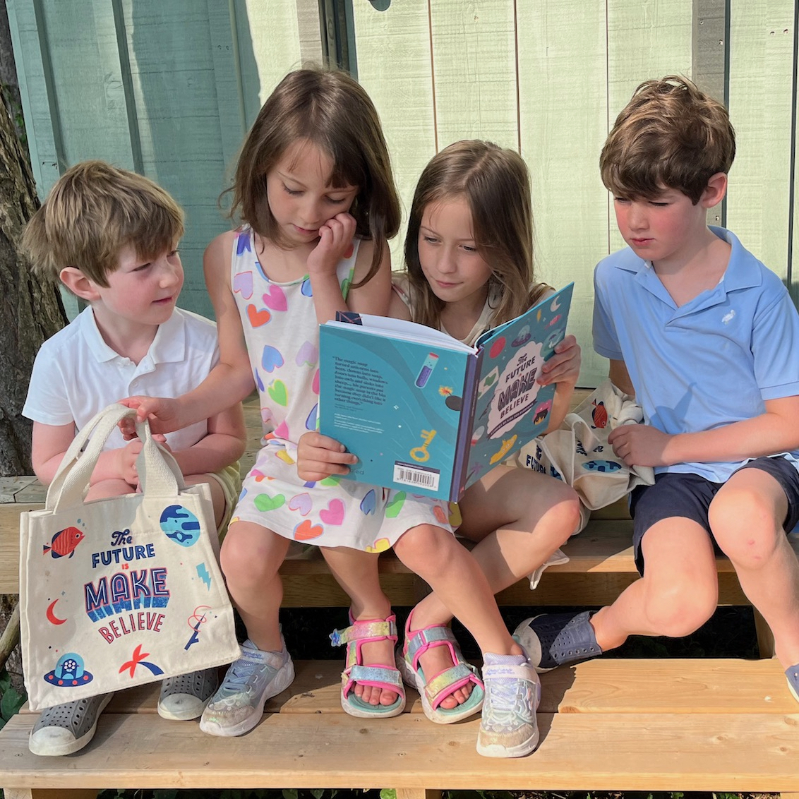 Children reading book of stories outside with small bag