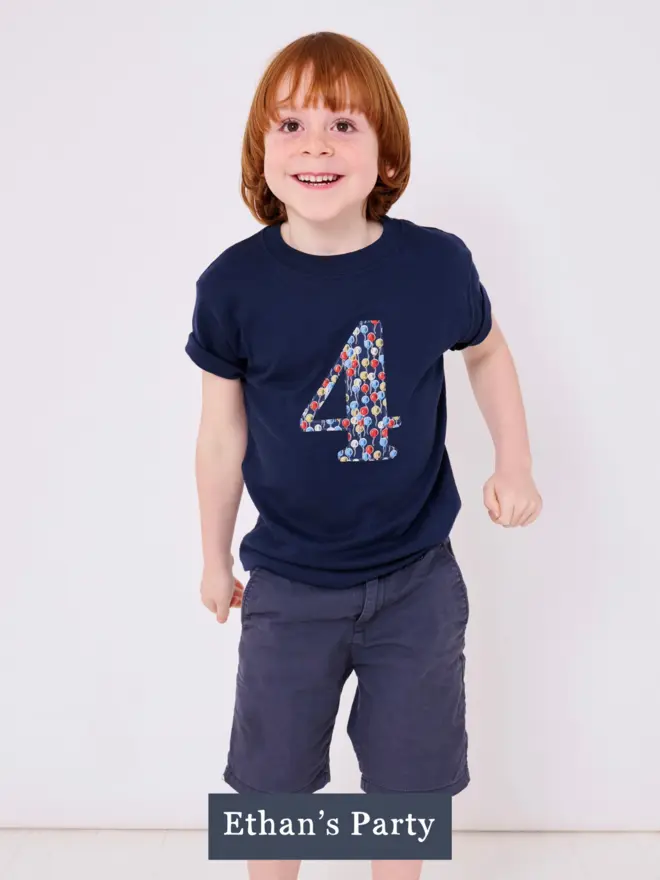 a 4 year old boy wearing a navy t-shirt with a balloon print number 4 on the front 